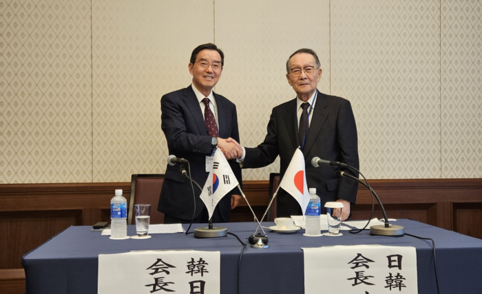 Korean and Japanese business leaders shake hands with flags displayed on table